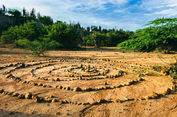 Labyrinth of stones spirals across the sandy landscape in Tatacoa Desert, Huila, Colombia, surrounded by lush green vegetation.