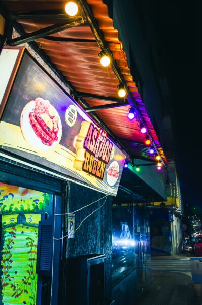 Vibrant storefront with colorful lights at night, featuring "Asados" signage in Santa Rosa de Cabal, Risaralda, Colombia.