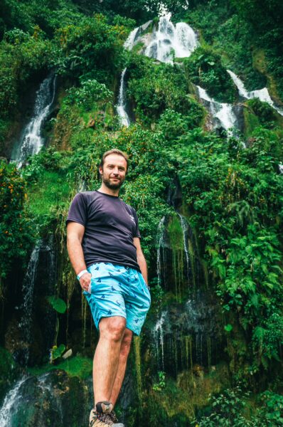 Man standing by cascading waterfalls surrounded by lush greenery at Termales Rosa in Risaralda, Colombia.