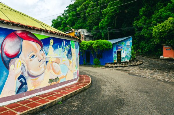 Colorful murals adorn the walls of hilly streets in Honda, Tolima, Colombia, surrounded by lush green foliage.