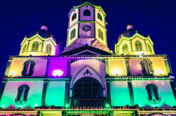 Illuminated Inmaculada Concepción church in Filandia, Quindío, Colombia, showcasing vibrant green and purple lighting at night.
