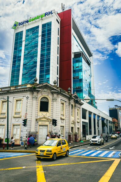 Modern glass buildings contrast with a historic colonial structure in Pereira, Risaralda, Colombia, busy with yellow taxis and traffic.