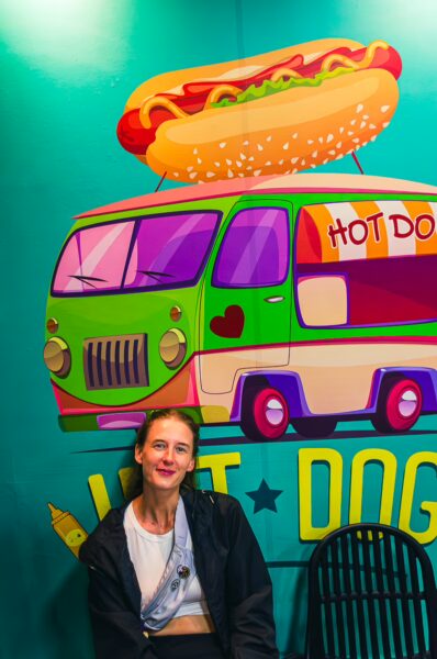 Brightly colored hot dog van mural with a woman sitting in front, showcasing vibrant art in Santa Rosa, Cabal, Risaralda, Colombia.
