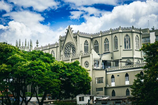 Gothic architectural details of Iglesia San José contrast with lush green trees in Pereira, Risaralda, under a blue sky.