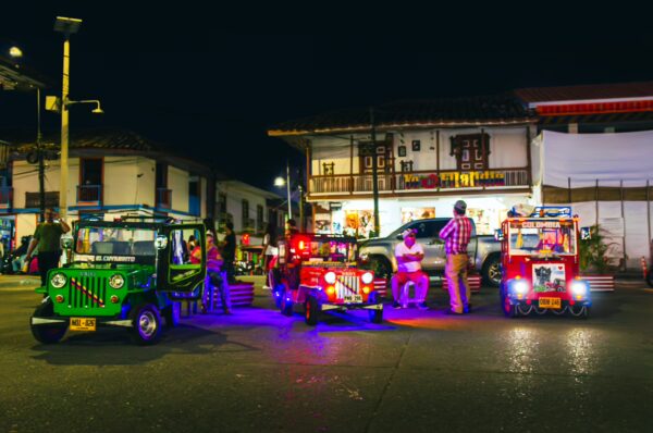 Vibrant tricycles with colorful lights gather in the lively streets of Parque Bolívar, Filandia, Quindío, Colombia at night.