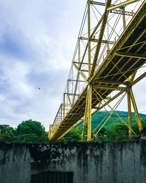 Vibrant yellow Puente Navarro stretches across a green landscape in Honda, Tolima, beneath a cloudy sky.