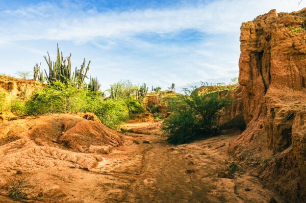 Vibrant red and orange hues form the rugged landscape of the Tatacoa Desert in Huila, Colombia, dotted with green vegetation.
