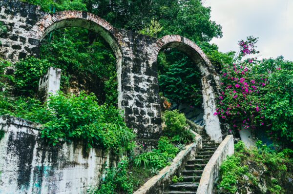 Arched stone structures covered in lush greenery and vibrant flowers lead up a winding staircase in Honda, Tolima.