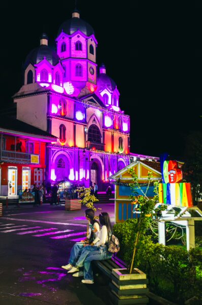 Colorful lights illuminate the historic architecture of Parque Bolivar in Filandia, Quindio, Colombia, as visitors relax nearby.