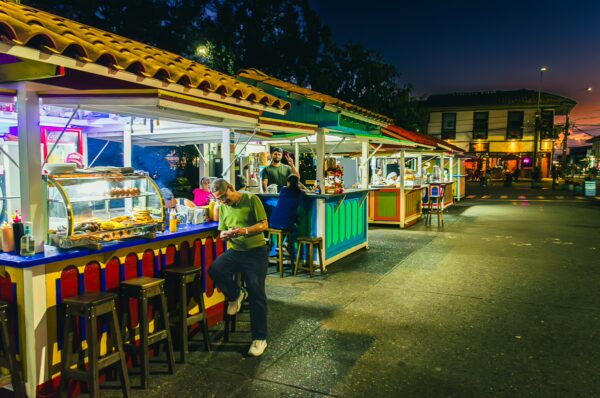 Vibrant food stalls line Parque Bolivar in Filandia, Quindio, Colombia, illuminated by colorful lights at dusk.