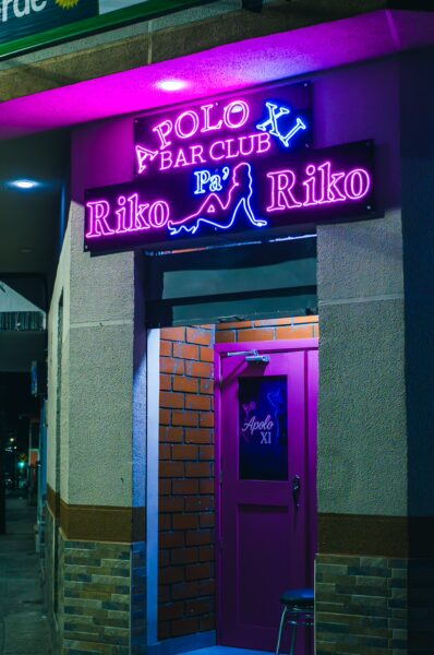 Vibrant neon sign for Riko Riko Bar Club illuminates the colorful entrance in Santa Rosa de Cabal, Risaralda, Colombia.