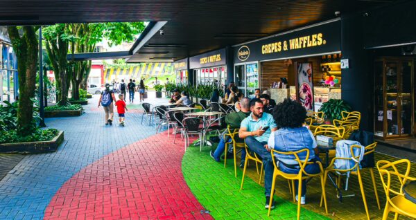 Colorful outdoor seating areas in Plaza Ciudad Victoria, Pereira, with people enjoying food and lush greenery surrounding the vibrant path.