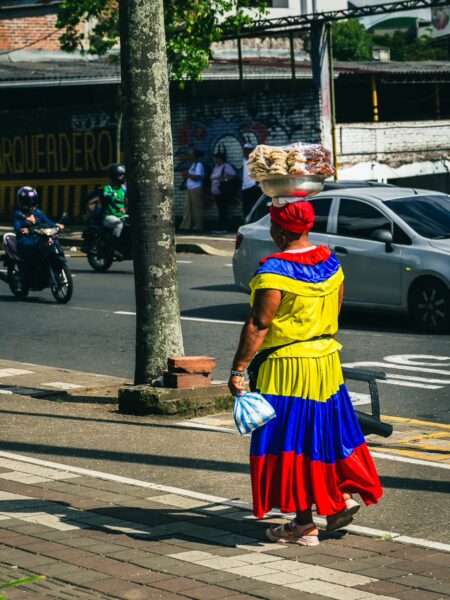 Colorful traditional dress in yellow, blue, and red worn by a woman walking in Plaza Ciudad Victoria, Pereira, Risaralda, Colombia.