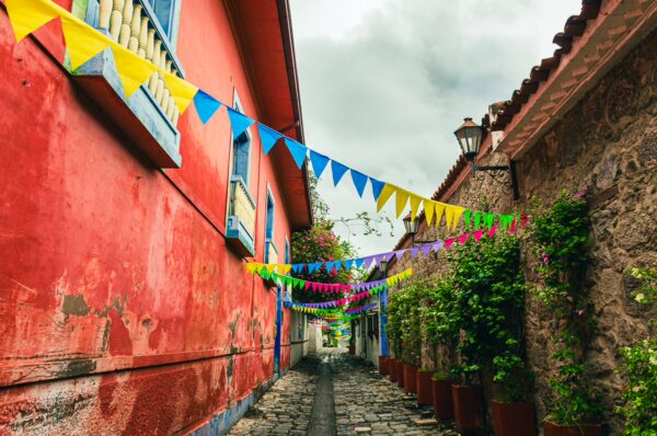 Brightly colored flags line the narrow Calle de las Trampas Honda in Tolima, Colombia, flanked by charming, colorful buildings.