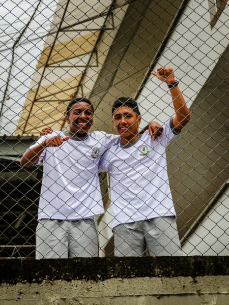 Two boys in white shirts cheer through a fence, capturing a joyful moment in Quindío, Colombia's vibrant atmosphere.
