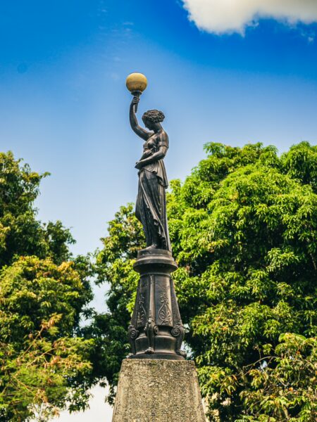 Elegant statue holding a globe, surrounded by lush greenery in Parque Olaya Herrera, Pereira, Risaralda, Colombia.
