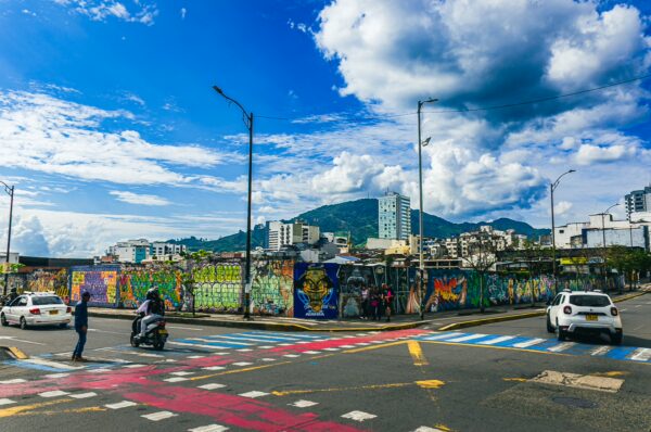 Vibrant street art covers a city wall in Pereira, showcasing colorful murals against a backdrop of cloudy skies and distant mountains.