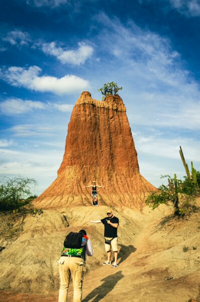 Red rock formations tower against a blue sky in Tatacoa Desert, Huila, Colombia, with visitors exploring the rugged landscape.