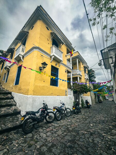 Vibrant yellow buildings line Calle de las Trampas Honda, with cobblestone streets and motorbikes adding charm in Tolima, Colombia.