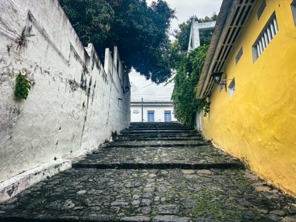 Stone steps lead up a vibrant yellow wall, flanked by white walls and lush greenery in Calle de las Trampas Honda, Tolima, Colombia.