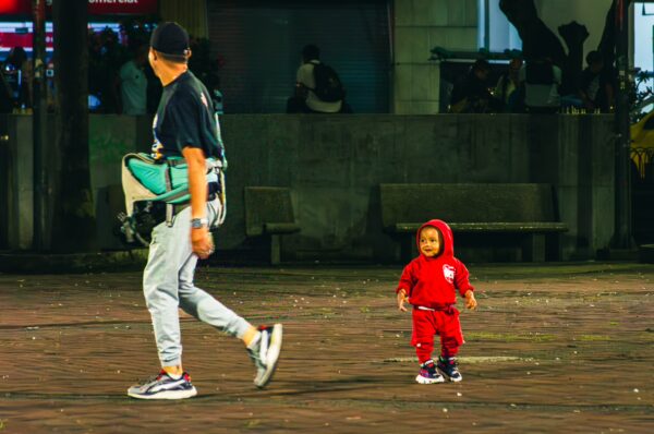Father and child walk together in Plaza de Bolívar, Pereira, Colombia, with vibrant city lights illuminating the scene.