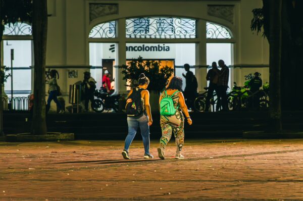 Two people walk through Plaza de Bolívar in Pereira, Colombia, with a lively crowd and storefronts in the background.