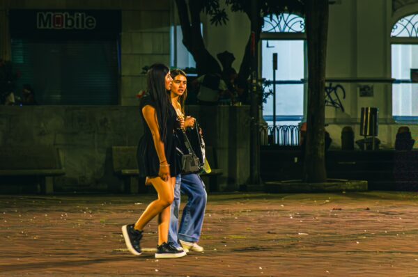 Two young women stroll through Plaza de Bolívar in Pereira, Risaralda, Colombia, under soft evening light.
