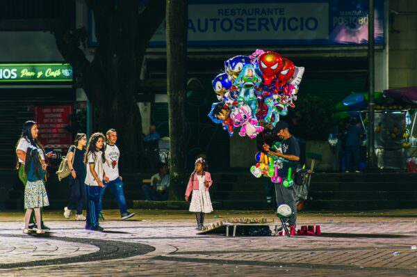 Colorful balloons fill the air as a vendor interacts with children in Plaza de Bolívar, Pereira, Risaralda, Colombia.
