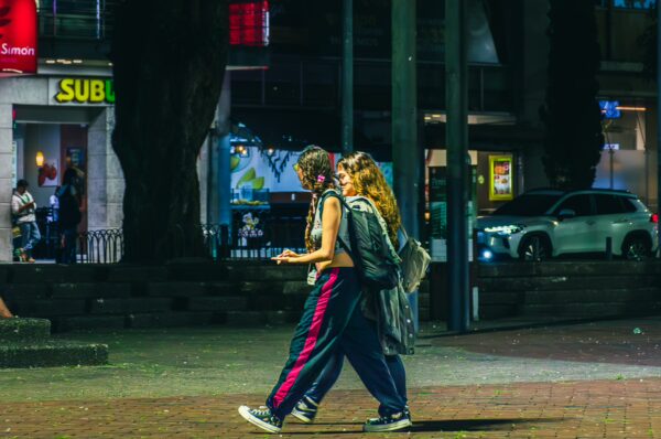 Young women stroll through Plaza de Bolívar, Pereira, Risaralda, Colombia, illuminated by city lights and nearby shops.