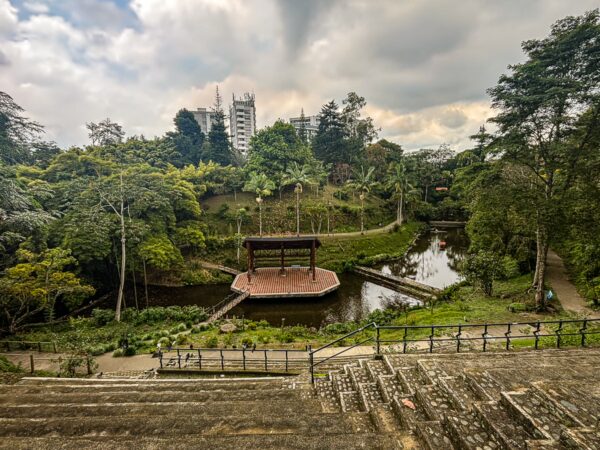 Lush greenery surrounds a tranquil pond and wooden gazebo at Parque de la Vida in Armenia, Quindio, Colombia.