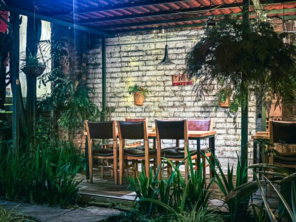 Cozy wooden dining area with a brick wall, surrounded by greenery in Pereira, Risaralda, Colombia. Soft lighting creates a warm ambiance.