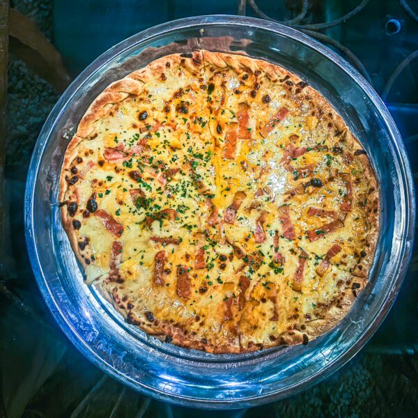 Delicious pizza topped with cheese and herbs, served on a glass plate, set against a dark wooden table in Pereira, Risaralda, Colombia.