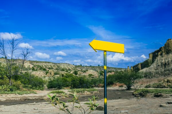 Yellow directional sign stands amid the arid landscape of Los Hoyos in the Tatacoa Desert, Huila, Colombia, under a blue sky.