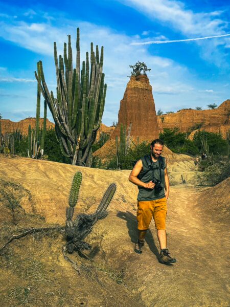 A traveler walks through the striking landscape of Tatacoa Desert, Huila, Colombia, with towering cacti and colorful rock formations.