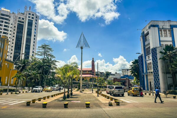 Modern buildings and palm trees line the street in Buenaventura, Valle del Cauca, creating a vibrant urban atmosphere under a sunny sky.