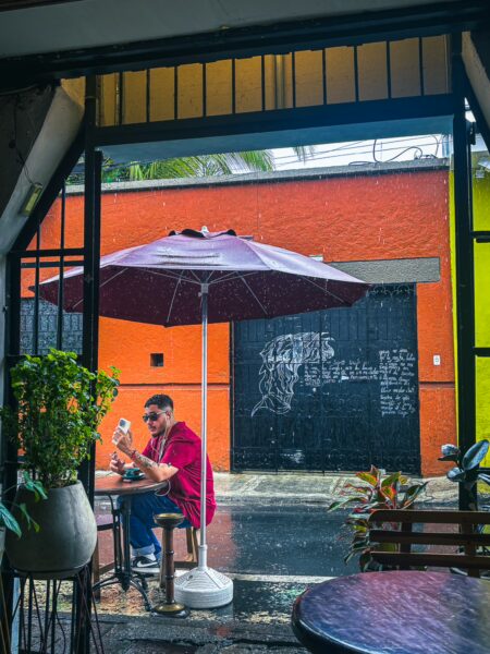 Colorful street scene in Cali, Valle del Cauca, Colombia, featuring a man under a purple umbrella enjoying a rainy day.