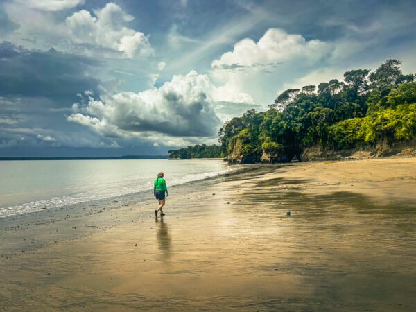 Serene Juan de Dios Beach features a solitary figure walking along the sandy shore, with lush greenery and dramatic clouds above.