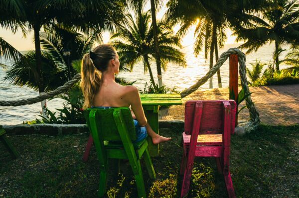 Sunset view from Ladrilleros, with a woman seated on colorful chairs, surrounded by palm trees and the ocean.