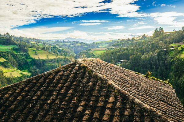 Stunning view of lush green valleys and rolling hills under a bright sky, with a rustic thatched-roof in the foreground, Las Lajas, Colombia.