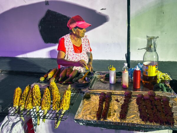 Colorful street food vendor at Parque Caldas, Popayán, Cauca, Colombia, showcasing grilled corn and meats under vibrant lighting.
