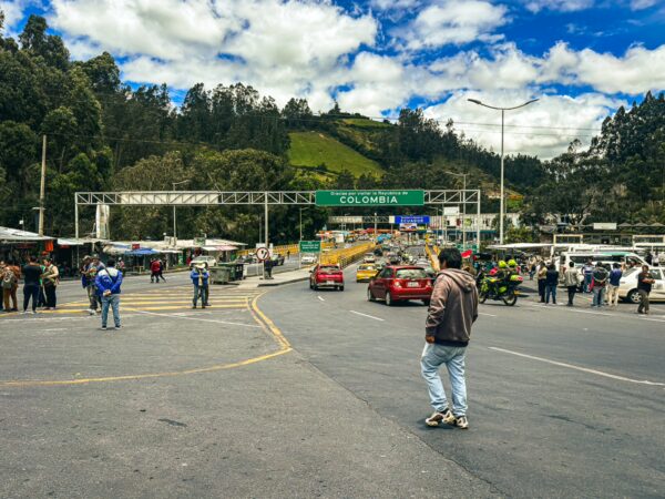 Busy border crossing at Rumichaca, showcasing vehicles, travelers, and vibrant greenery under a bright sky in Nariño, Colombia.