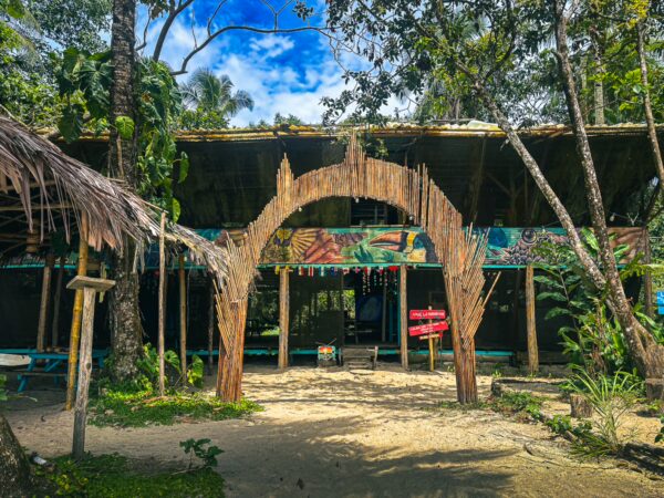Colorful entrance with a thatched archway surrounded by lush greenery, leading to Juan de Dios Beach in Uramba, Bahia Malaga, Colombia.