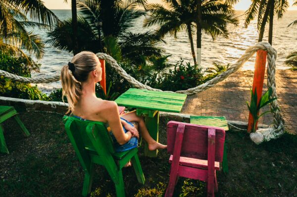 Brightly colored green and pink chairs overlook the sunset at Ladrilleros, Valle del Cauca, Colombia, with palm trees in the background.