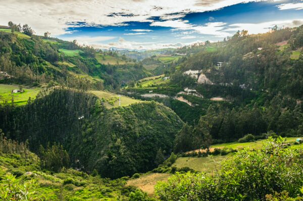 Lush green hills and valleys showcase the vibrant landscape of Las Lajas, Nariño, Colombia, under a bright blue sky.