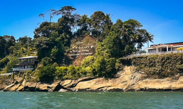 Maguipi features a lush, green hillside with a sign and a coastal view along Valle del Cauca, Colombia.