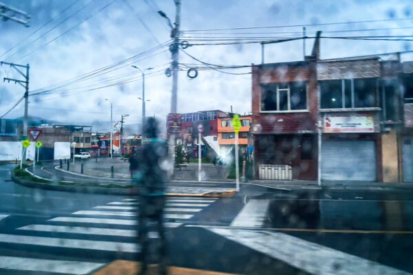 Raindrops blur the view of a street in Pasto, Nariño, Colombia, featuring traffic signage and nearby buildings.