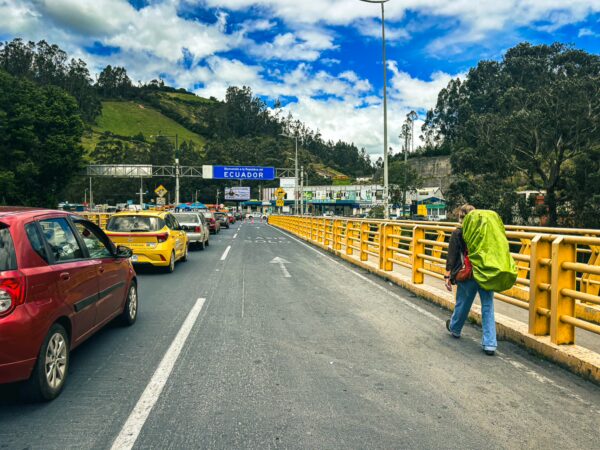 Traffic fills the rumichaca border crossing, with bright yellow barriers and lush green hills under a blue sky in Narino, Colombia.