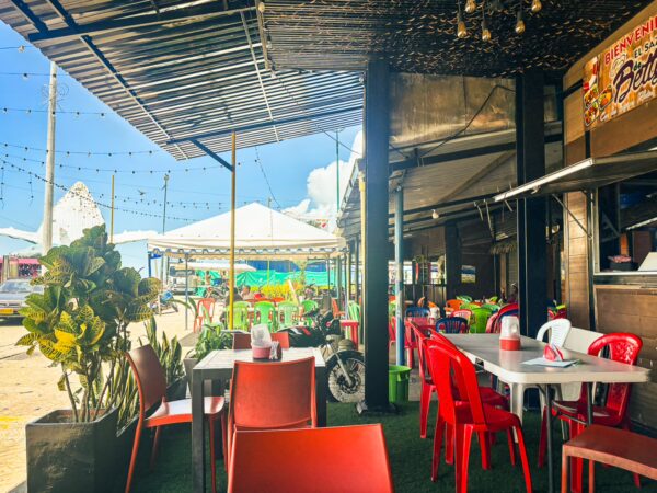 Vibrant outdoor dining area with red chairs, tables, and green plants, set against a sunny backdrop in Buenaventura, Valle del Cauca, Colombia.