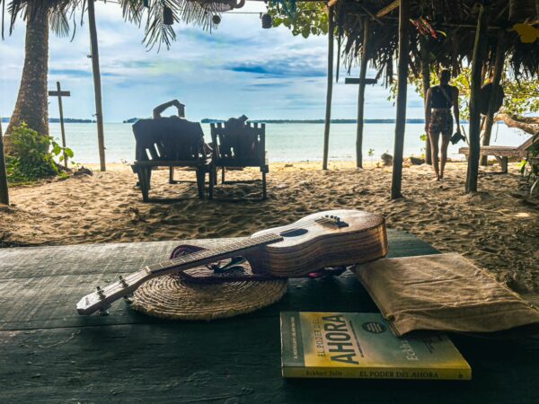 Relaxing scene at Juan de Dios Beach, featuring a guitar on a table, books, and a view of the tranquil Uramba Bahia in Valle del Cauca.