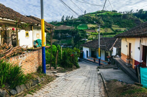 Charming cobblestone street lined with white and colorful houses, greenery, and rolling hills of Narino, Colombia.